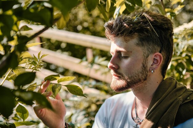 Portrait of a young blond man smelling some green leaves in a park in spring