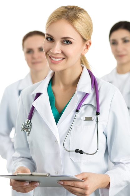 Portrait of young blonde female doctor holding file with documents surrounded by medical team, looking and smiling. Healthcare and medicine concept.