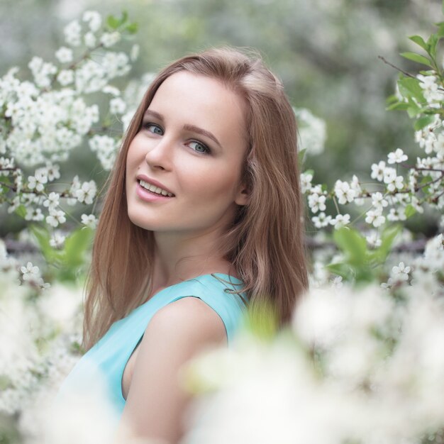 Portrait of a young blonde girl in a blue dress. apple trees in flowers.