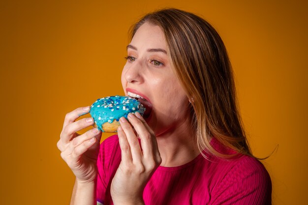 Portrait of a young blonde girl eating a delicious colorful donuts.