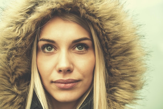 portrait of young blonde girl wearing winter jacket with a hood on head isolated over white background