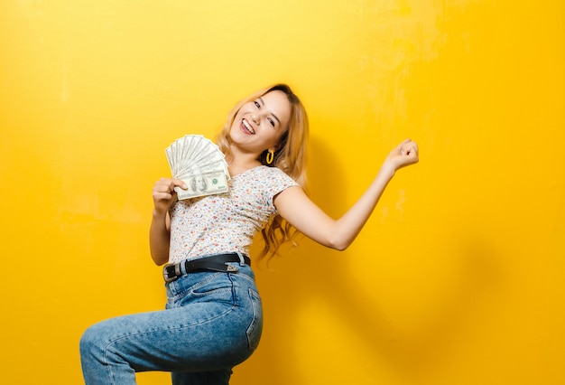 Ritratto di una giovane ragazza bionda felice tenendo le banconote sul muro giallo