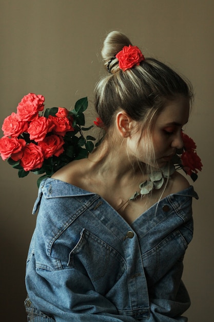 Portrait of a young blonde with red makeup in a denim jacket and a bouquet of roses