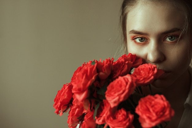 Photo portrait of a young blonde woman with red makeup and a bouquet of roses