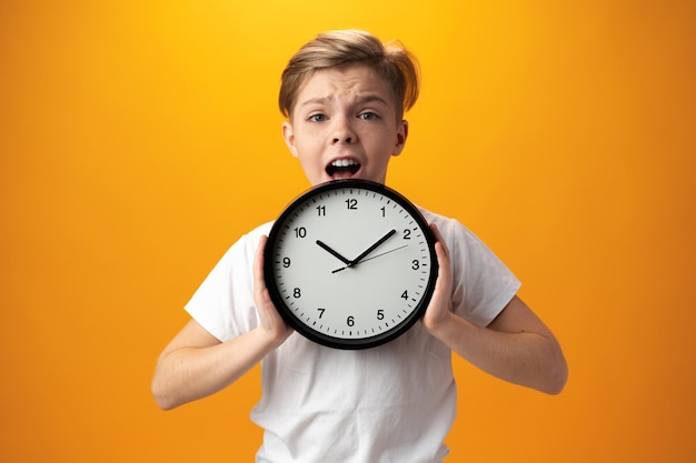 Portrait of a young boy holding a clock against yellow background