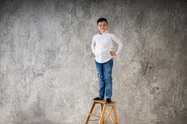 Portrait of a young boy standing on a chair isolated on a white background in the studio