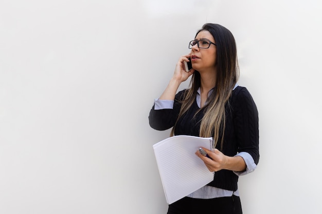 Portrait of a Young Brunette Business Woman holding a mobile pencil and notebook Isolated on White Background