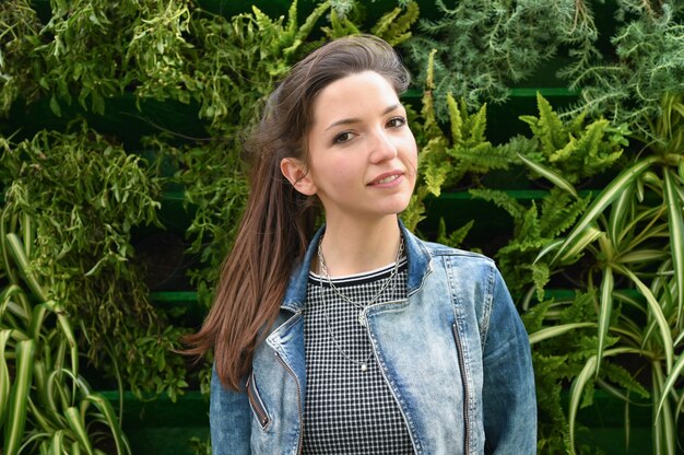 Portrait of a young brunette girl in a denim jacket. against the space of green plants