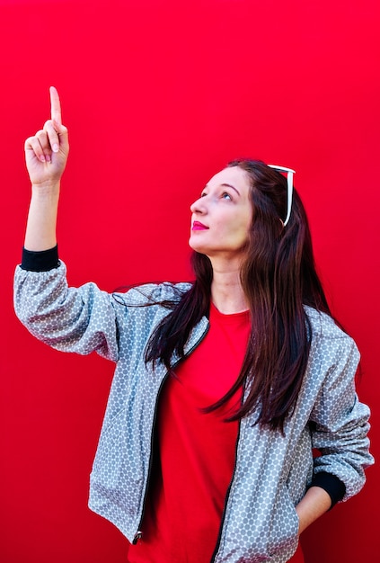 Portrait of a young brunette girl pointing up on flat red background