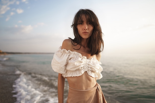 Portrait of young brunette haired woman at the beach at sunset