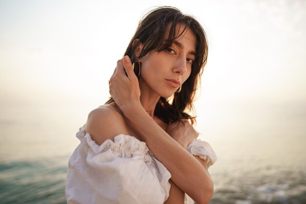 Portrait of young brunette haired woman at the beach at sunset