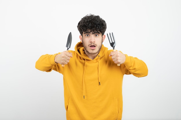 Portrait of a young brunette man standing and holding garden tools .