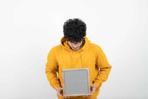 Photo portrait of a young brunette man standing and holding gray frame .