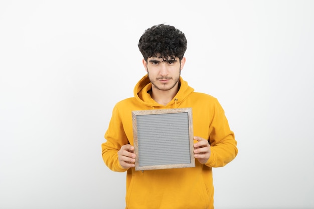 Portrait of a young brunette man standing and holding gray frame .