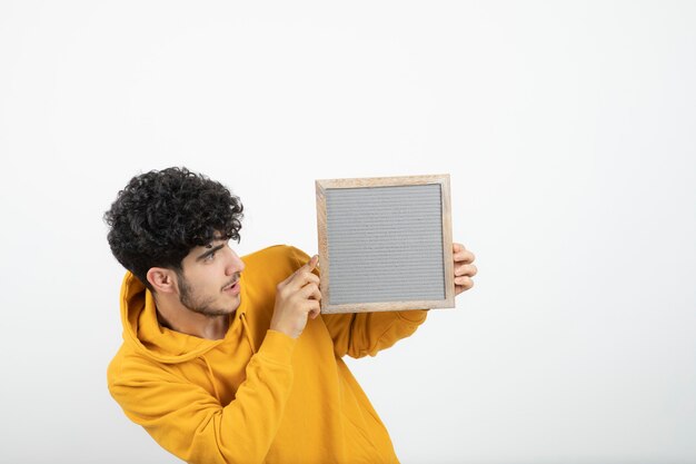 Portrait of a young brunette man standing and holding gray frame .