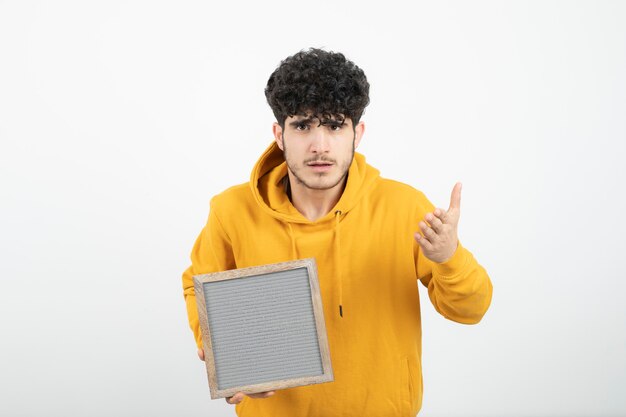 Portrait of a young brunette man standing and holding gray frame .