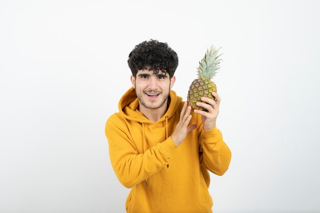 Portrait of a young brunette man standing and holding pineapple .