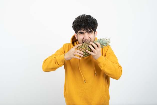 Портрет молодого человека брюнет стоя и держа ананас.