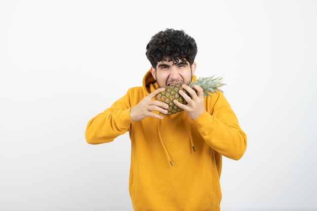 Portrait of a young brunette man standing and holding pineapple .