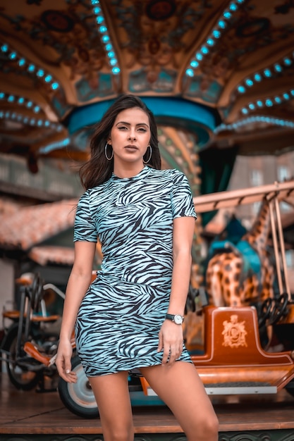 portrait of A young brunette sitting in tight dress on a merry-go-round at the fair, looking to the right