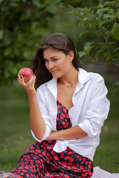 Foto ritratto di una giovane bruna con una mela in un giardino estivo. foto di alta qualità