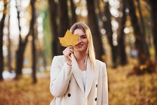 Portrait of young brunette with leaf that is in autumn forest at daytime.