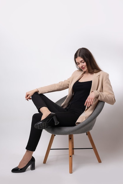 Portrait of a young brunette with long hair in the studio Cute girl sitting on a chair on a white background