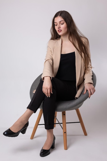 Portrait of a young brunette with long hair in the studio Cute girl sitting on a chair on a white background