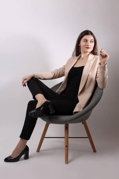 Portrait of a young brunette with long hair in the studio Cute girl sitting on a chair on a white background