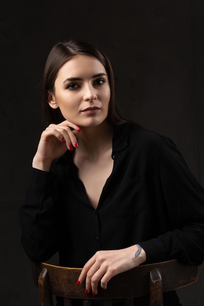 Portrait of a young brunette with long hair in the studio Dramatic photo in dark colors A girl with a snake tattoo on her arm