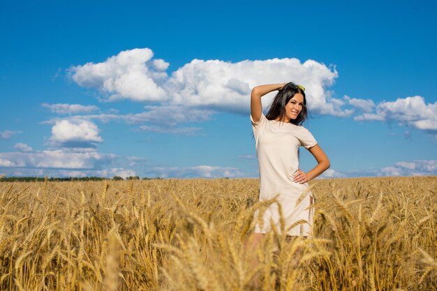 Portrait of a young brunette woman on a background of golden wheat field summer outdoors