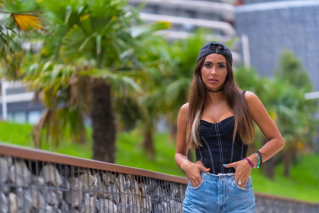 Portrait of a young brunette woman in a black cap and jeans in the city