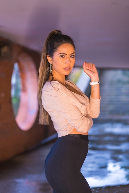 Portrait of young brunette woman in the city with a beautiful ponytail and a short pink sweater