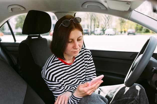 Portrait of a young brunette woman driving in a car using a smartphone