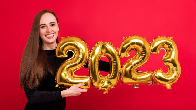 Portrait of a young brunette woman holding the numbers of the new year 2023 on a red background Panoramic photo