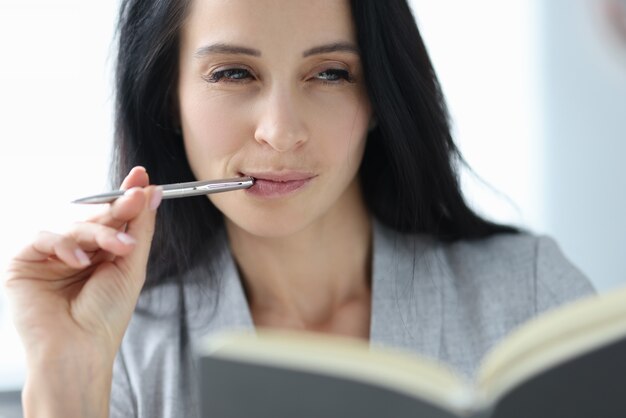 Portrait of young brunette woman with ballpoint pen in her mouth. Journalism concept