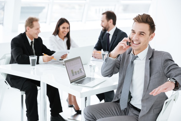Portrait of young business man sitting by the table with colleagues and talking at phone