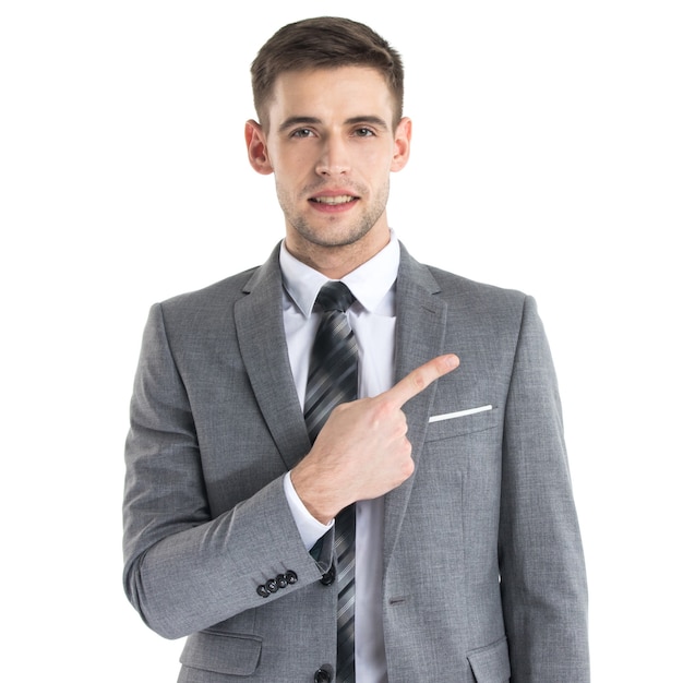 Portrait of young business man in suit pointing aside at copy space over white wall