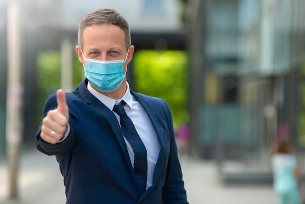 portrait of young business man with mask holding thumbs up