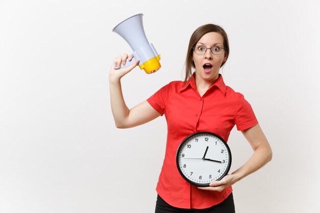 Portrait of young business teacher woman in red shirt holding round clock, scream in megaphone, announces discounts sale, isolated on white background. Hot news, communication concept.. Hurry up, guys