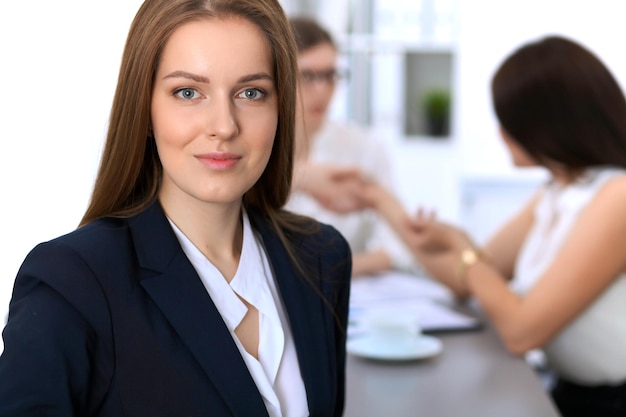 Portrait of a young business woman against a group of business people at  meeting.