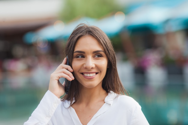 Portrait of a young business woman dressed in a white blouse while talking on the phone outdoors