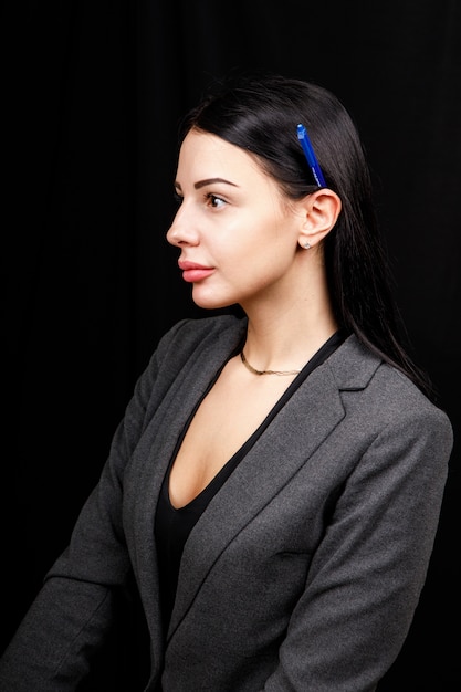 Портрет молодой деловой женщины в серой куртке на черной космической ручке за ухом.