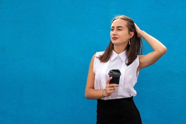 Portrait of young business woman holding cup of coffee isolated on blue