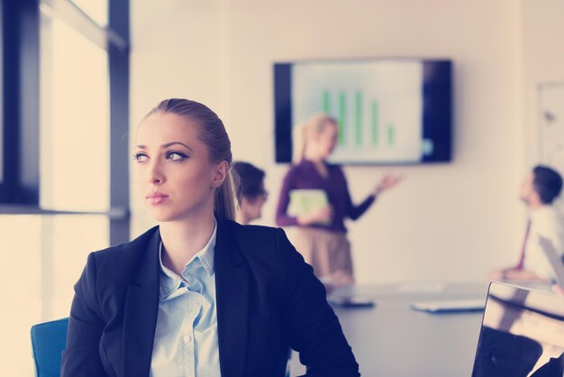 Portrait of young business woman at modern startup office
interior, team in meeting group in background