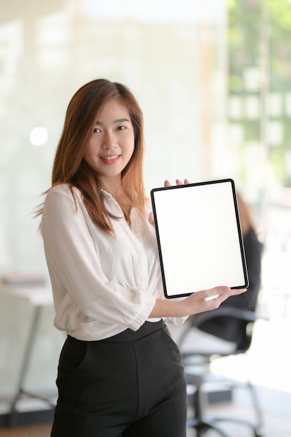 Portrait of young business woman showing blank screen digital tablet while standing in office room