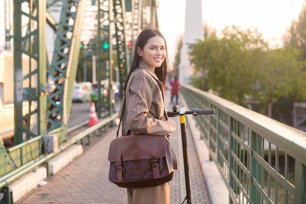 Portrait of young business woman with an electric scooter to work over bridge