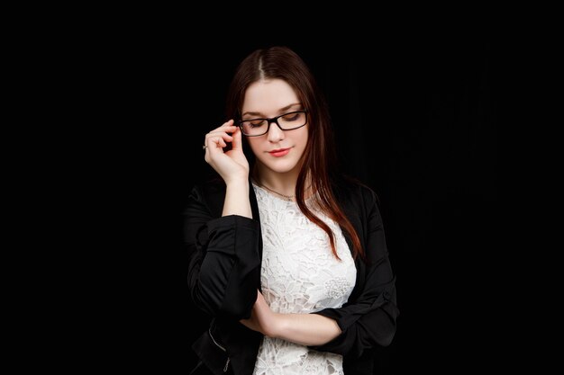 Portrait of young business woman with glasses in a black jacket on black.