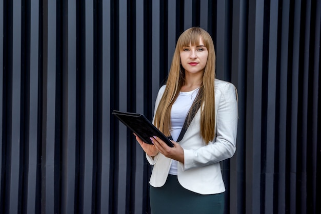 灰色の壁の上のタブレットを持つ若いビジネス女性の肖像画