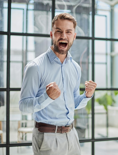 Photo portrait of a young businessman in a blue shirt shaking his fists celebrating his success